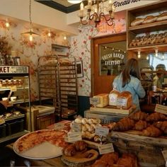 a woman standing in front of a bakery counter filled with breads and pastries