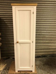 a tall white cabinet sitting on top of a wooden floor next to a garage door