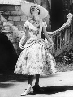 a woman in a dress and hat is standing outside