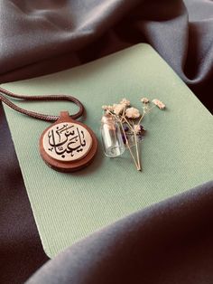 a necklace with an arabic writing on it next to a flower in a glass jar