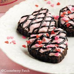 three heart shaped cookies on a plate with chocolate drizzle and pink icing