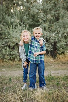 two young boys standing next to each other in front of some trees and grass with their arms around each other