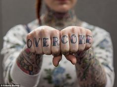 a man with tattoos on his arms holding up the word overcome in front of him