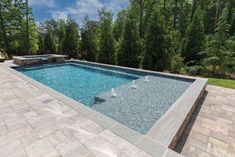 an empty swimming pool surrounded by stone pavers and brick walkways with trees in the background