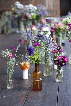 several vases filled with different types of flowers on a wooden table, all lined up