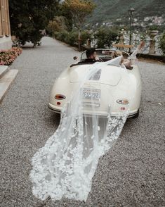 a bride and groom ride in an old fashioned sports car with a veil draped over it