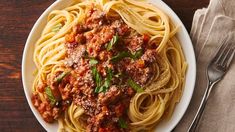 a plate of spaghetti with meat sauce and parmesan cheese on the side next to a fork