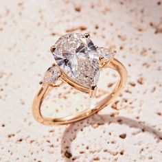 three pear shaped diamonds on a yellow gold ring, set against a textured background