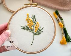 a hand holding a embroidery hoop with yellow flowers on it