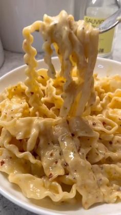 a fork full of macaroni and cheese being lifted from a white bowl with water in the background