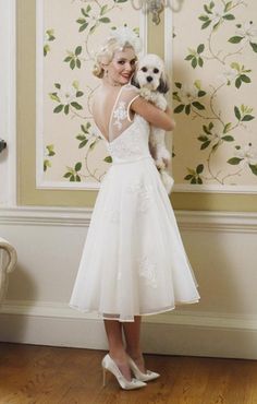 a woman in a white dress is holding a small dog and posing for the camera