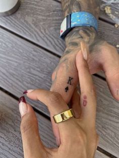 two people holding hands with tattoos on their fingers and one has a gold band around the wrist