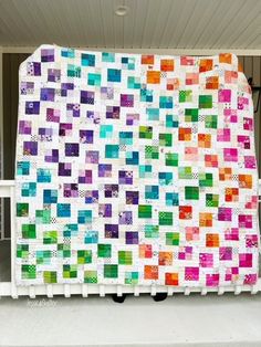 a colorful quilt hanging from the side of a building with white railings on it