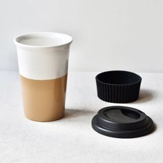 a coffee cup next to a black lid on a white tablecloth with a small object in the foreground