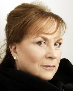 a woman with red hair wearing a black scarf and looking off to the side, in front of a white background