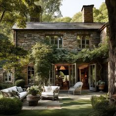 an outdoor patio with chairs and tables in front of a stone house surrounded by trees