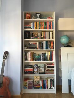 a book shelf filled with lots of books next to a guitar