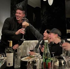 two men and one woman are toasting with wine glasses in front of them at a dinner table