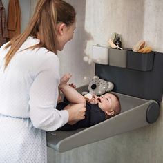 a woman standing next to a baby in a sink with a teddy bear on the wall