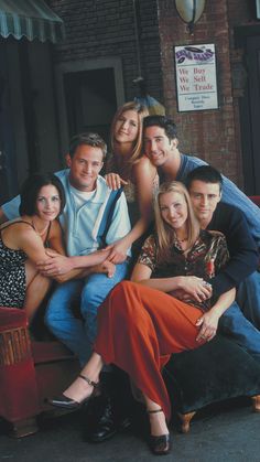 a group of people sitting next to each other on top of a couch in front of a brick wall