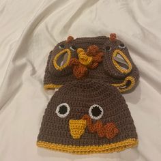 two crocheted hats are laying on a white sheet, one is brown and the other is yellow