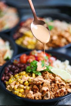 a spoon drizzling sauce over a bowl of mexican food with beans and corn