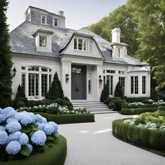 a white house with blue flowers in the front yard