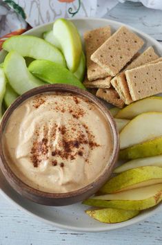 a white plate topped with apples and crackers next to an apple slice, dip