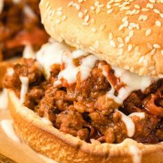 a sloppy joe sandwich with cheese and meat in it on a wooden cutting board next to other food items