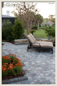 an empty lounge chair sitting on top of a brick patio next to a flower garden