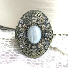 Beautiful vintage brass filigree statement dinner ring with elegant rhinestones and a gorgeous bezel set round, light blue and beige Agate cabochon stone in the center.  The ring is large measuring 1 3/4 inches long X 1 3/8 inches wide and fitting a ladies finger size  7 1/4 US.   This ring is in great condition showing some minimal patina from the normal aging process, such as some darkening of the brass. Please be sure to look closely at all pictures as I do try to capture the items condition Luxury Ornate Cabochon Ring, Dinner Ring, Brass Filigree, Lady Fingers, Costume Rings, Round Light, Agate Cabochon, Aging Process, Agate Stone