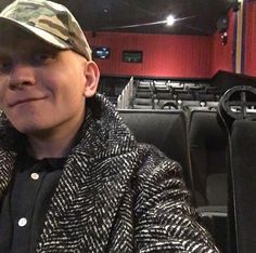 a man wearing a hat and jacket sitting in front of an auditorium filled with seats