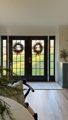 a living room filled with furniture and christmas wreaths on the front door window sill