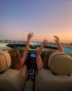 two people sitting in the back seat of a car with their hands up to the sky