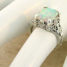 a white ring with an opal surrounded by filigrees on it's sides