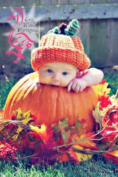 a baby wearing a knitted pumpkin hat sitting on top of a pile of leaves