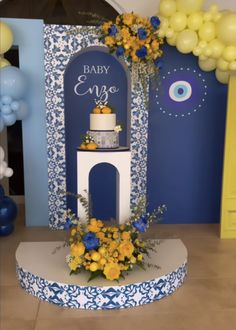 a blue and white baby shower with yellow flowers on the cake stand in front of it