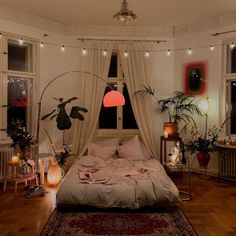 a bedroom with lots of plants and lights on the wall above the bed, in front of two windows