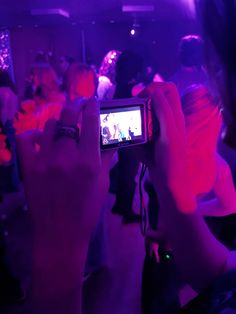 a person taking a photo with their cell phone in front of purple lights at a party