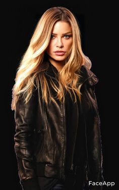 a woman with long blonde hair wearing a black leather jacket and looking at the camera