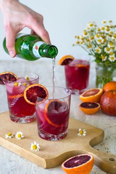 a person pours wine into glasses filled with blood orange slices and garnished with daisies