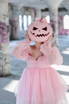 a woman in a pink dress with a pumpkin on her head