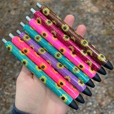 a hand holding five different colored pencils in it's palm, which are decorated with sunflowers