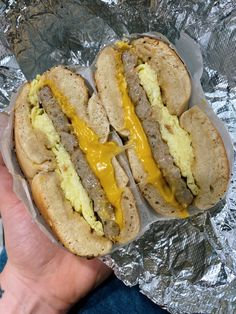 a hand holding a hot dog covered in cheese and meat on tin foil with other food items