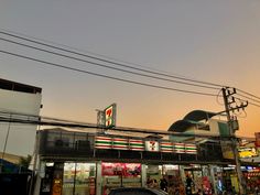 a car is parked in front of a convenience store at sunset or sunrise, with people walking on the sidewalk