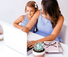 a mother and daughter sitting at a table with a laptop