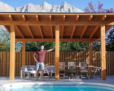 a man standing in front of a swimming pool under a pergolated roof with mountains in the background