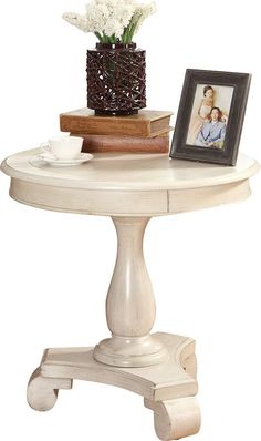 a white table with a vase and flowers on it next to a framed photo, coffee cup and books