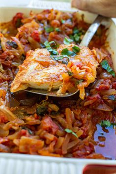 a white dish filled with pasta and meat covered in sauce, garnished with parsley