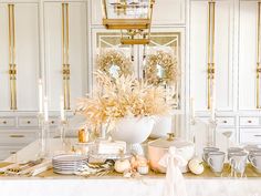 a white table topped with lots of plates and bowls filled with food next to tall gold chandeliers